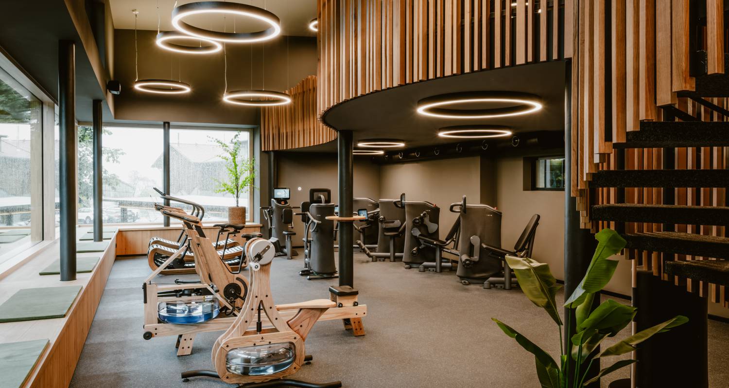 Hotel-Fitnessraum mit Rudergeräten aus Holz, Indoorbikes und runden Deckenleuchten vor einer Fensterfront