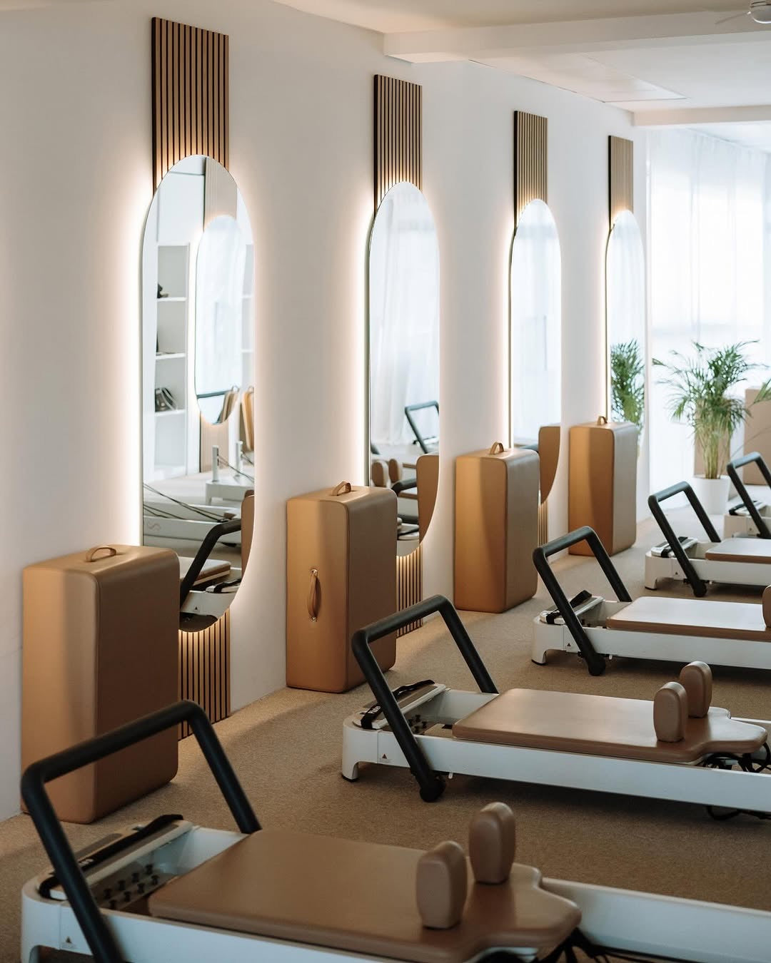 Pilates-Studio mit einer Reihe Reformer aus hellem Holz vor bogenförmigen Spiegeln