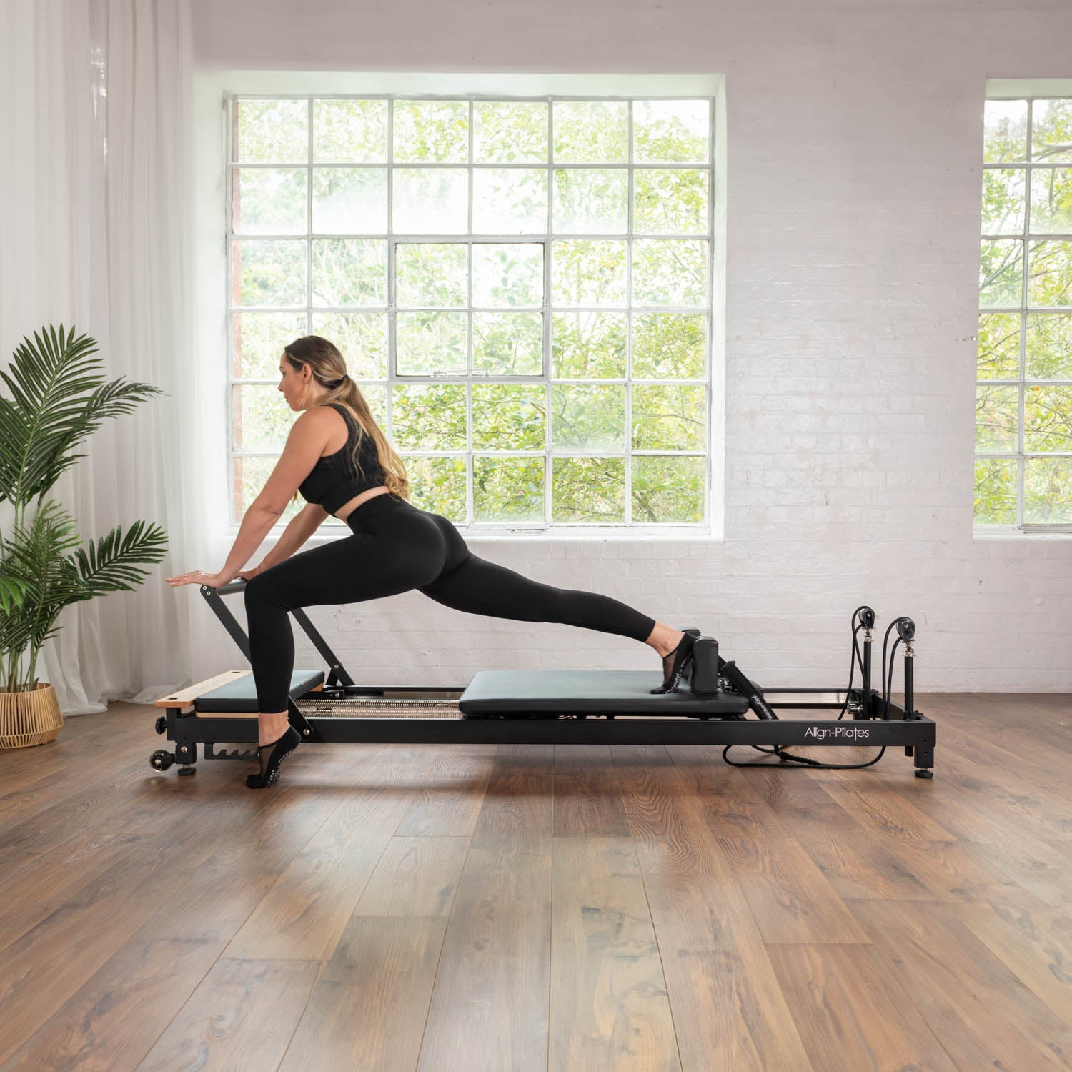 Frau bei einer Lunge-Übung auf dem Align Pilates R8-Pro Reformer in Schwarz
