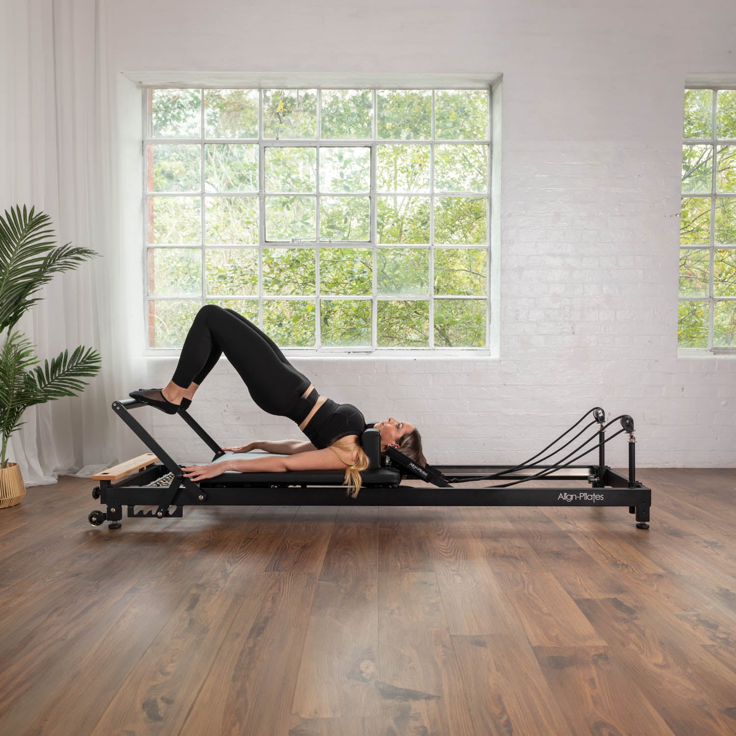Frau bei einer Bridge-Übung auf dem Align Pilates R8-Pro Reformer in Schwarz